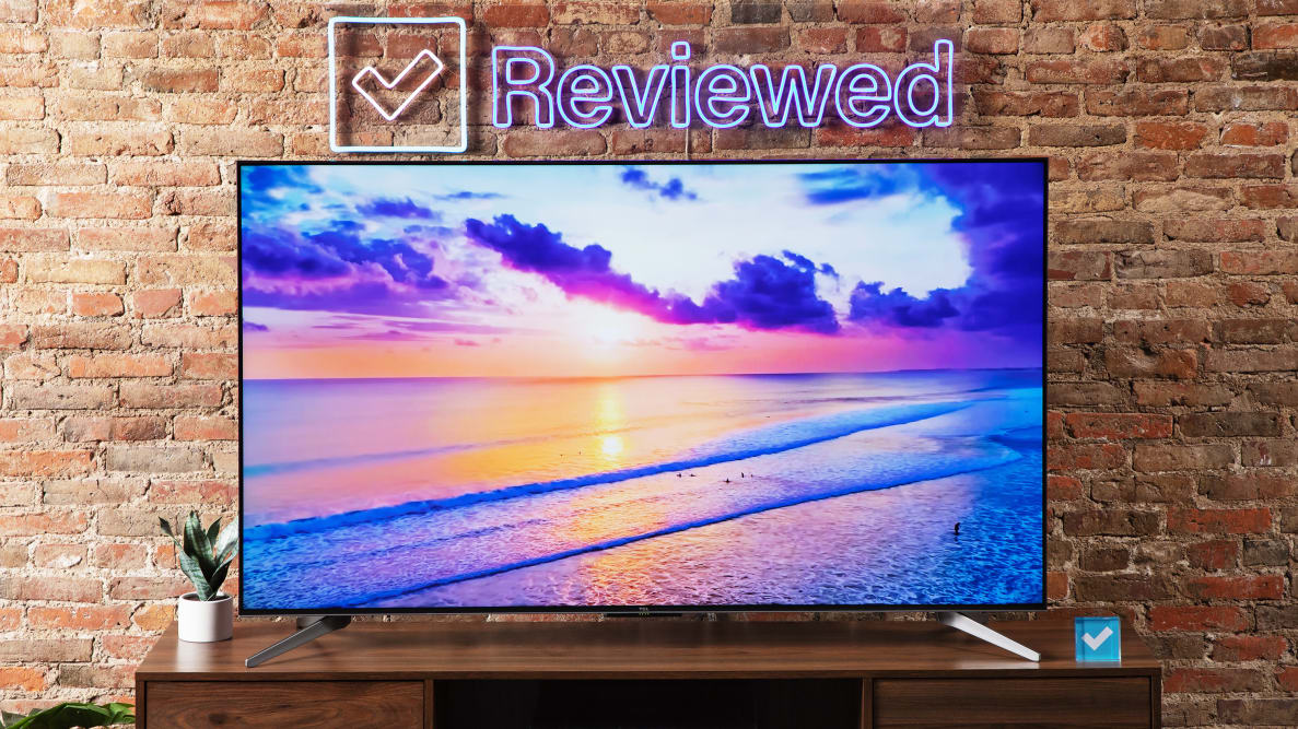 TCL Q7 QLED TV on an entertainment center, with a brick background and Reviewed sign above the TV.