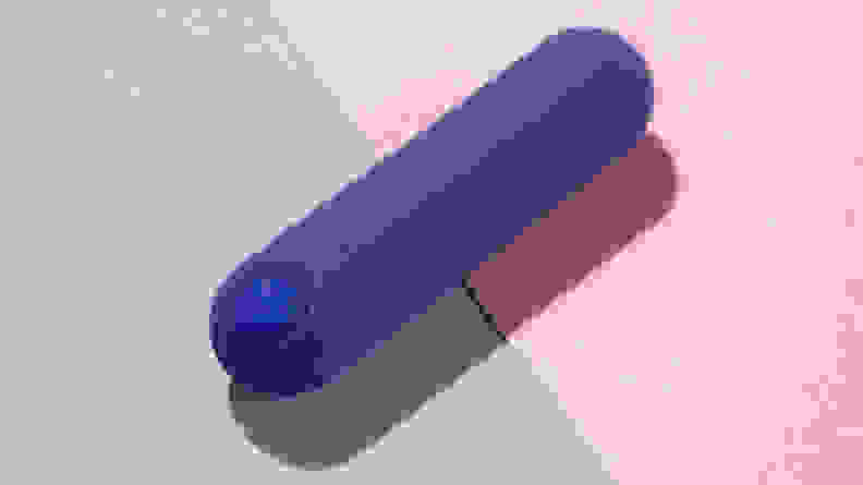 A dark blue PlusOne Bullet Vibrator on top of a pink and purple background.