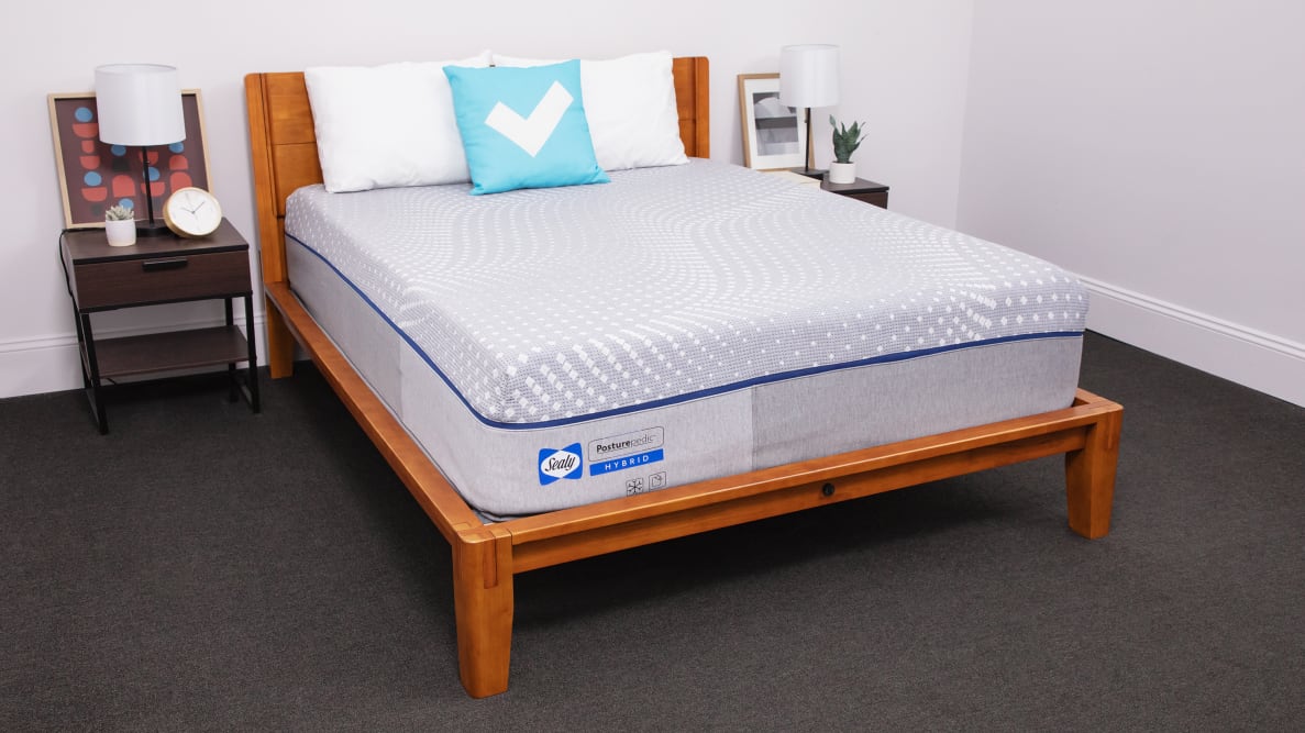 The Sealy Posturepedic mattress inside of a wooden frame with two pillows on top indoors.