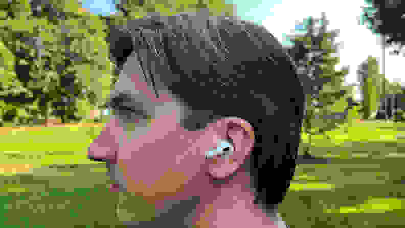 A man in a green park listens to a white AirPods Pro earbud.