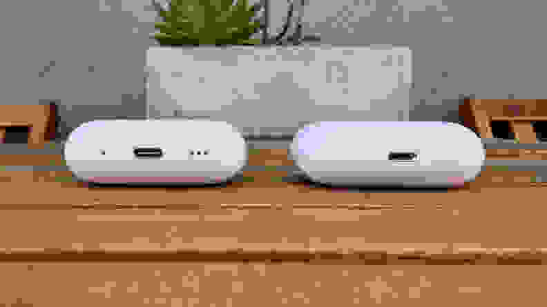 The two white AirPods Pro cases sit next to each other on a wooden table.