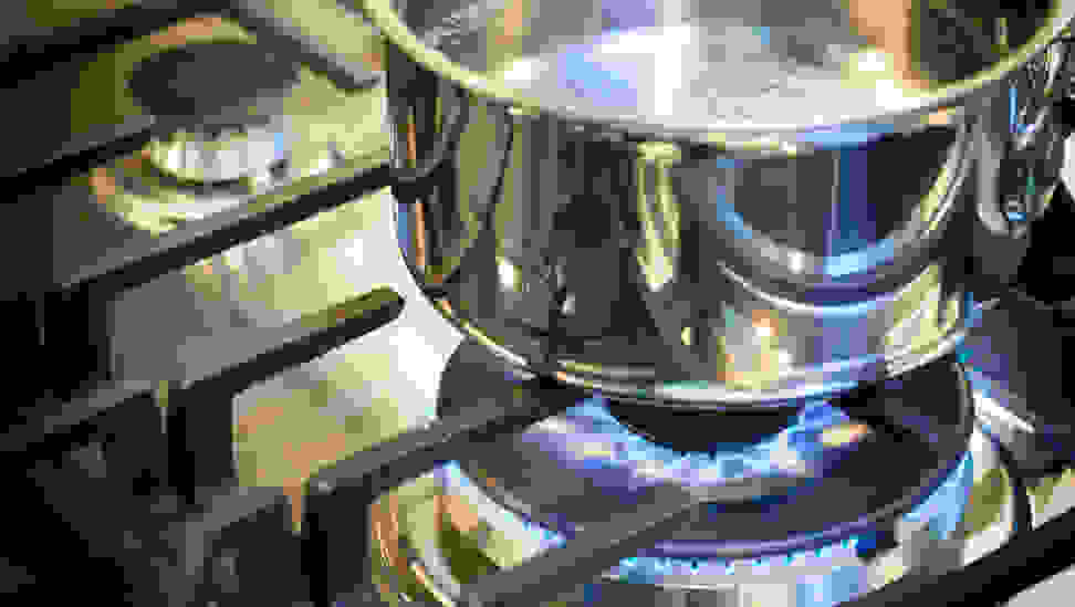 A pot of water sit on the burner of a gas stove with the flame on below it.