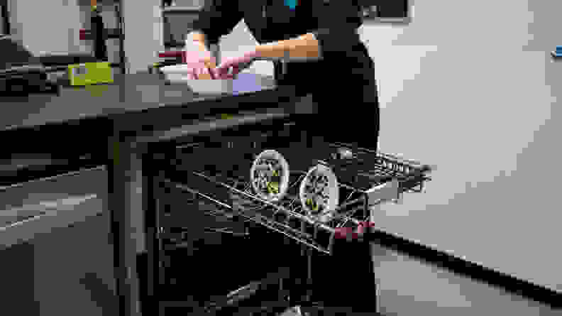 Two white bowls covered in pureed spinach sit in the top rack of a dishwasher