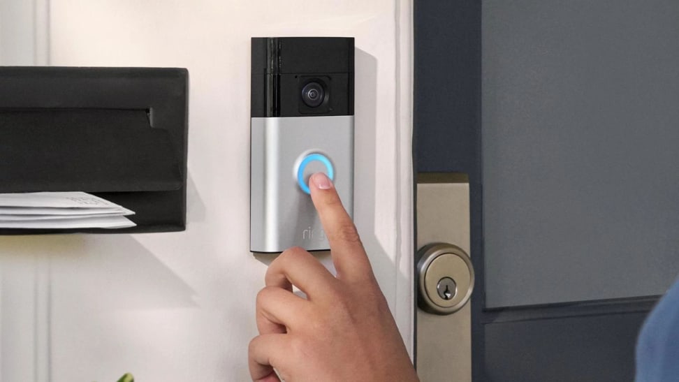 A person’s finger presses the chime button on the new Ring Battery Doorbell that is hanging on the exterior of a home