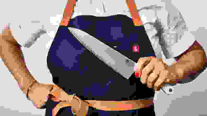 Person wearing navy apron and holding chef's knife from Hedley & Bennett.