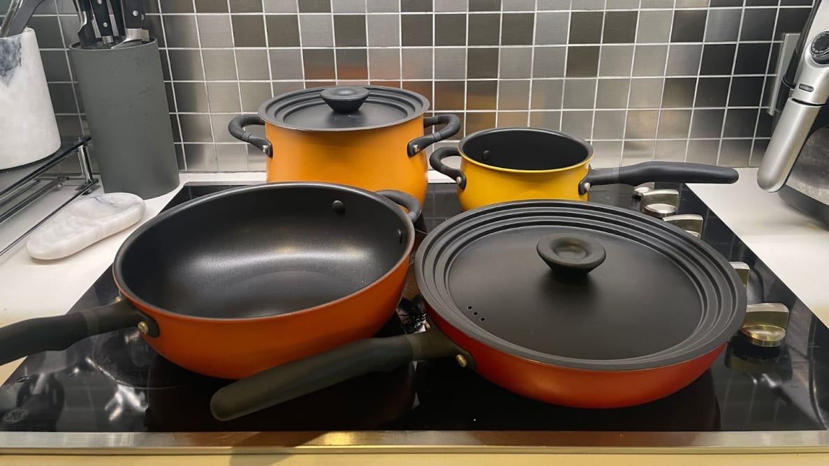 Orange, red, yellow Meyer skillets and pots sitting on top of cooktop in kitchen.