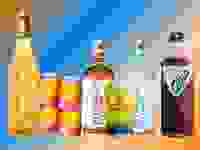 Non-alcoholic wine, mixers, beer, spirits, and cocktails are arranged in a row over a colorful blue and orange gradient background.