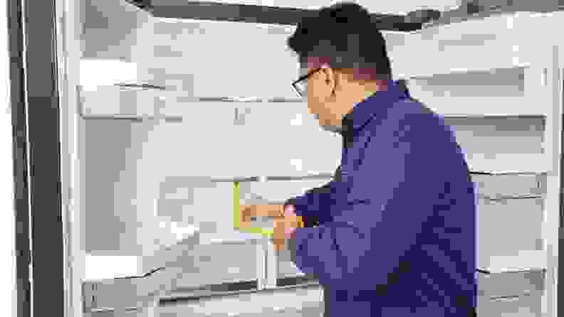 Lab technician measures shelf height inside of refrigerator with measuring tape.