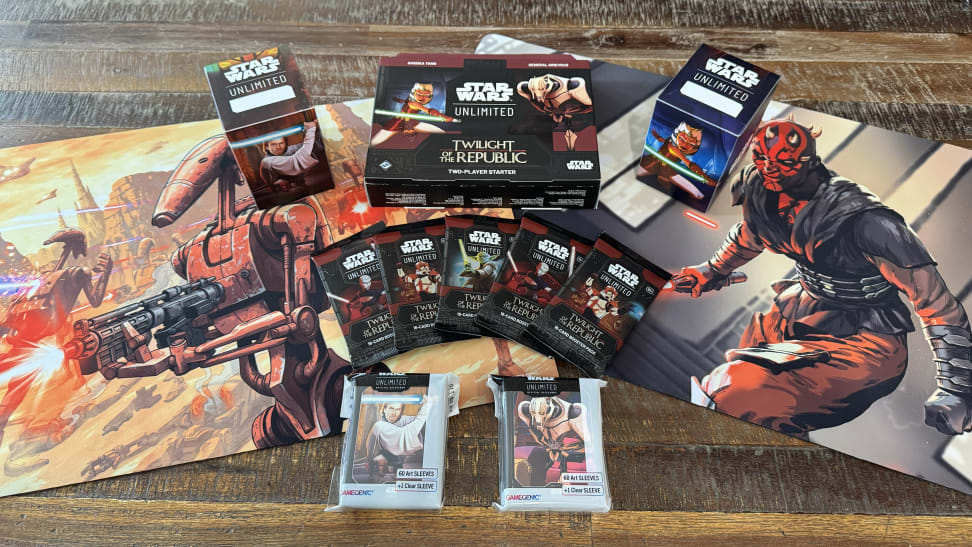 The Star Wars: Unlimited card game, with cards fanned out in front of a deck of cards, cardboard tokens, two deck boxes with images of Luke Skywalker and Darth Vader, the game box with the same images, and a foldable playmat.