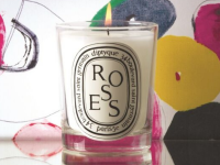 A lit Diptyque candle sits on a table.