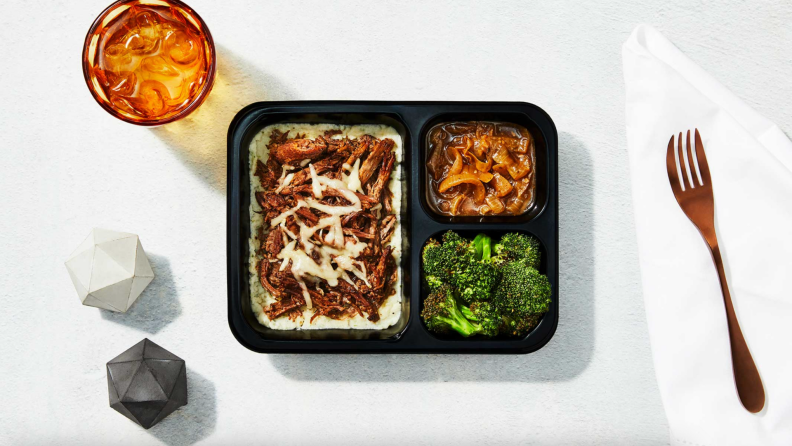 A Factor prepared meal besides a fork and cup of water on white surface