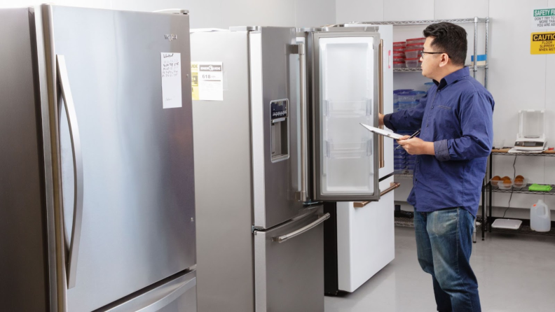 A man stands in our testing labs with a clipboard, holding the door of a fridge open.