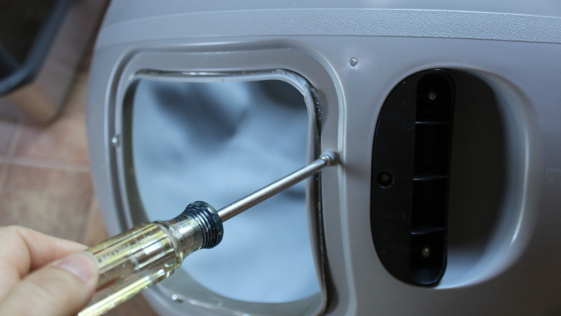 Someone using a screwdriver to remove screws on the Litter-Robot globe.