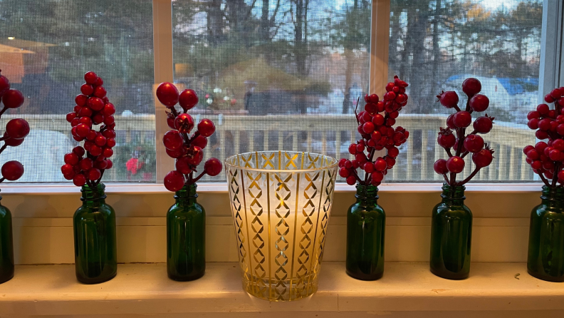 A candle on a window sill with jars filled with winter berries.