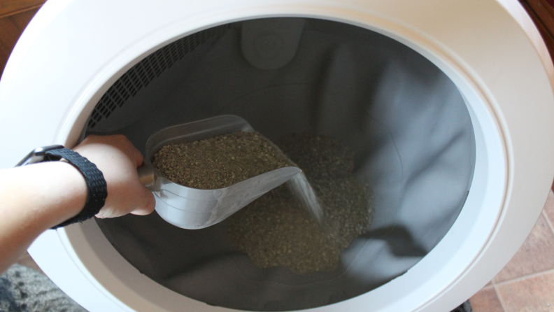 A woman’s hand holding a scoop and putting litter into the Litter-Robot.