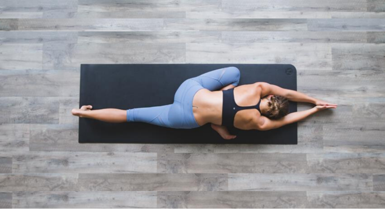 A woman is in a half pigeon yoga pose. The view is from the ceiling.