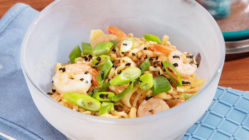 Cooked ramen with shallots, sesame seeds and shrimp inside of clear microwavable bowl.