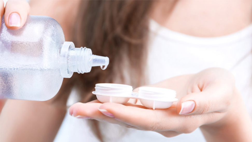 Close-up of a person applying solution to contacts in a contact case.