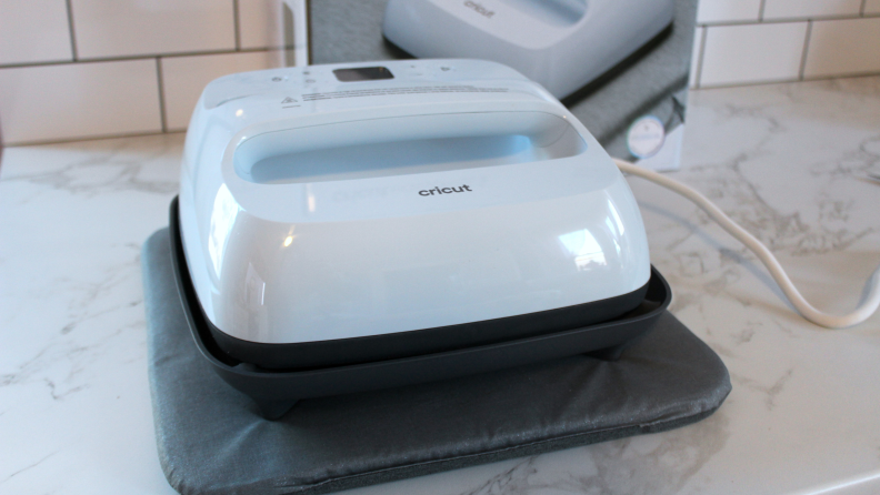 A Cricut heat press on a gray padded material atop a white countertop.