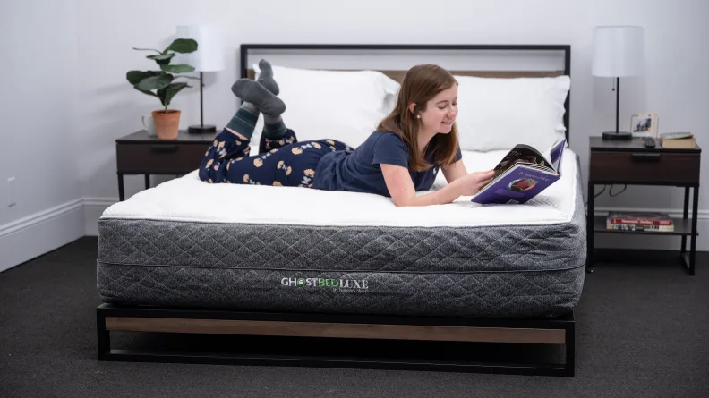 A woman wearing pajamas reads a book while lounging on a mattress.