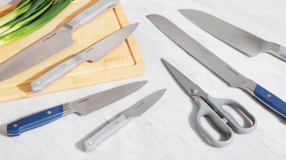 Misen knife set is spread on a marble counter and wood cutting board with scallions in the background.