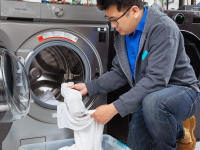 An Asian man pulls white socks and towels out of a washing machine