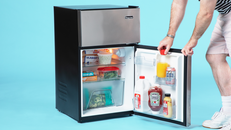 A close-up of someone opening the fridge compartment of the Magic Chef HMDR31GSE mini fridge. It's fully stocked with food.