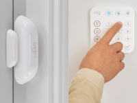 On left, white oval sensor on window panel. On right, person using finger to press buttons on alarm system keypad.