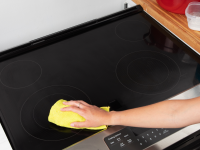 A person wipes a glass stove top with a rag.