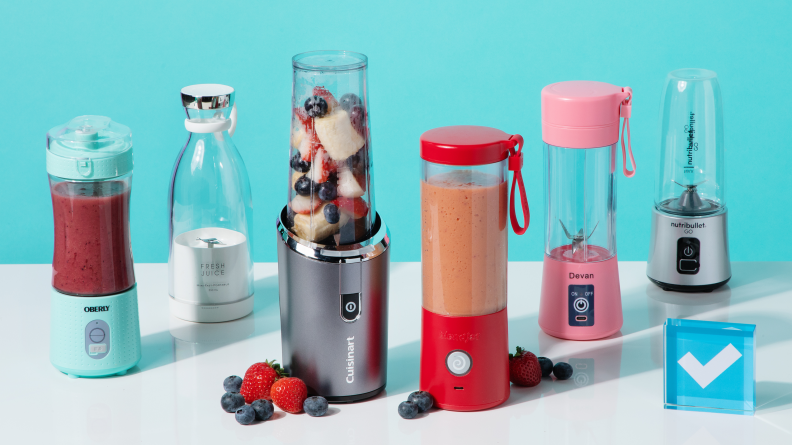 Six portable blenders sit on a white surface surrounded by berries.