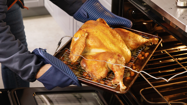 A person taking a roast spatchcock turkey from the oven.