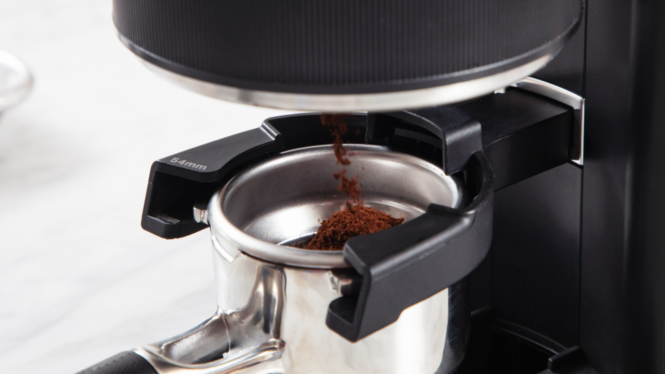 A close-up of a grinder ejecting coffee grounds into an espresso portafilter