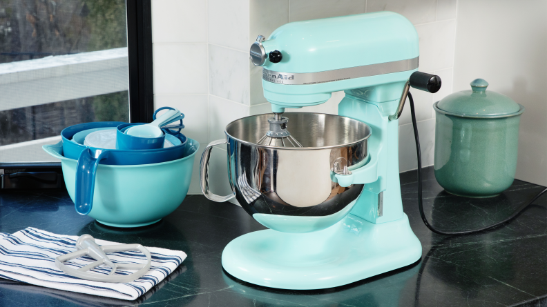 A teal KitchenAid 600 stand mixer sits on a black counter with blue mixing bowls and a cookie jar.