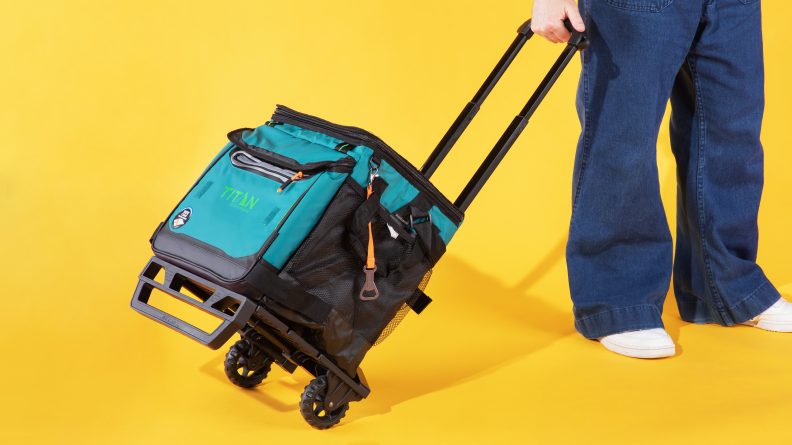 A soft cooler on wheels being pulled against a yellow background