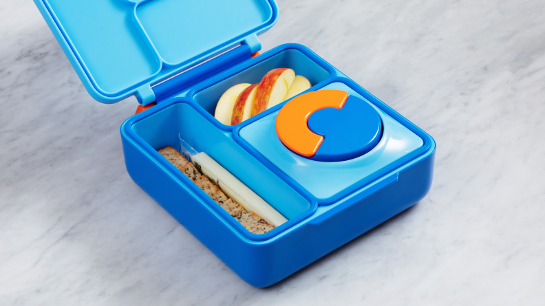 The OmieBox sits open on a marble counter with its Thermos in place and food in two compartments.