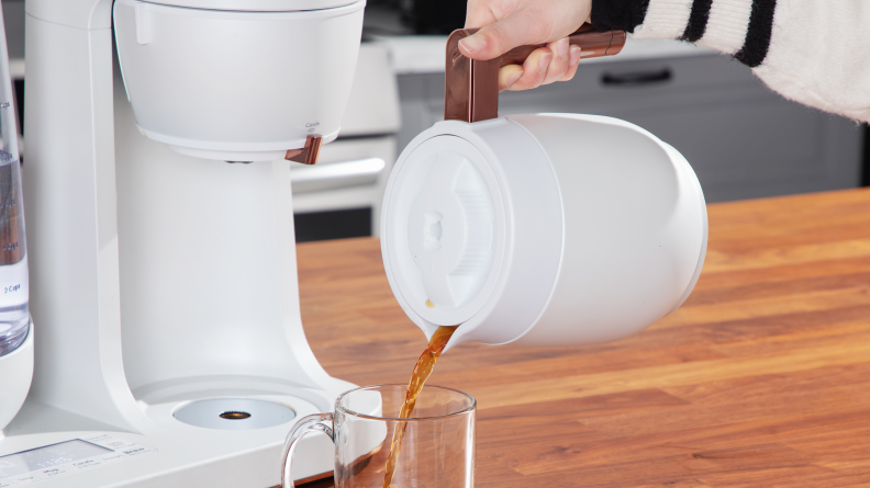 A person pouring black coffee into a clear mug from a white canister.