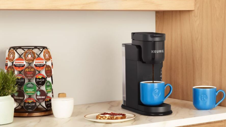 Keurig machine brewing coffee beside a tower of K-cups