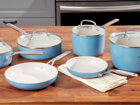 Blue and white pans and pieces from the KitchenAid cookware set sitting atop a wooden table.