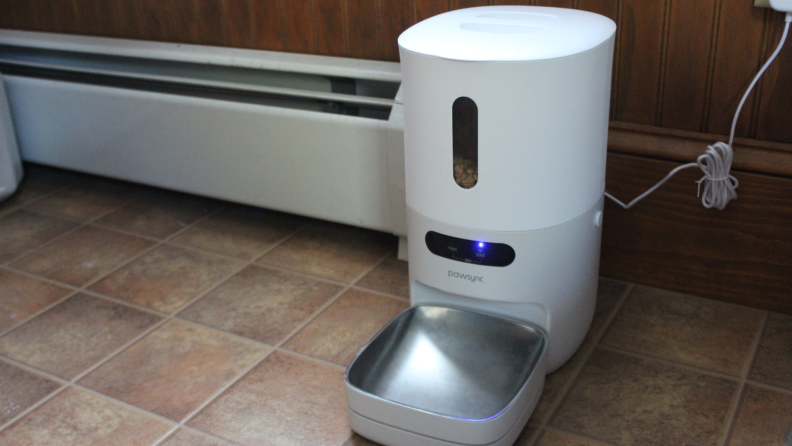 The PawSync Smart Pet Feeder on a tile floor plugged into a wall.