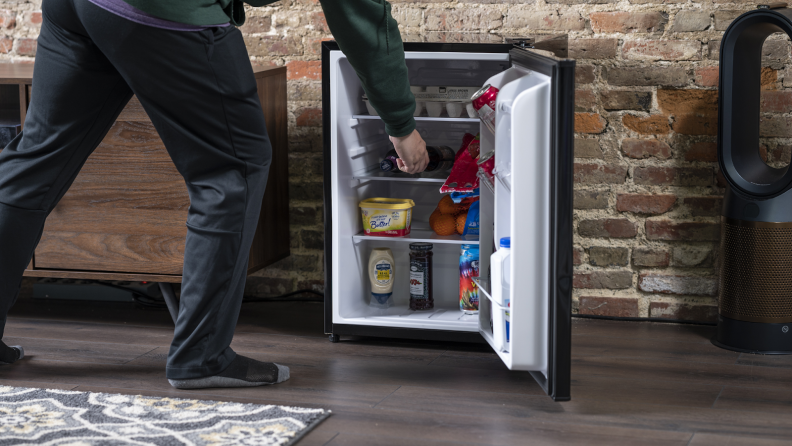 A close-up of someone reaching into a fully stocked mini-fridge.