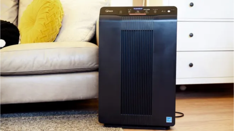 A Winix air purifier next to a sofa and dresser.