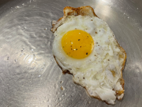 An egg cooked on a stainless-steel pan.