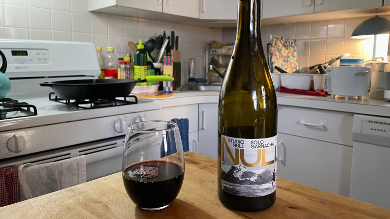 A half-full wine glass and a bottle of Studio Null's Solo Garnacha sitting on a kitchen counter.