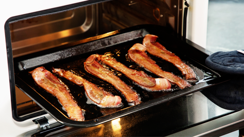 Six strips of cooked bacon on a small baking sheet being removed from an air fryer.