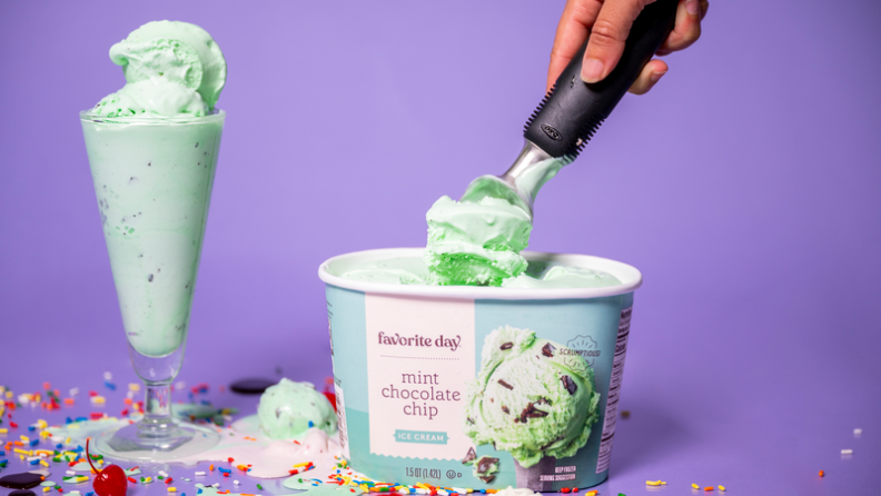 An OXO scoop digging into a pint of mint chocolate chip ice cream, with a filled ice cream cup beside it.